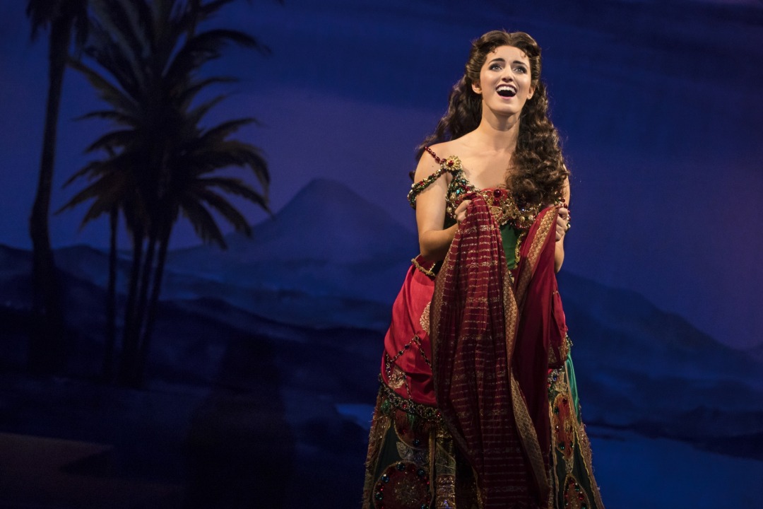 Christine in a red and green beaded dress in front of a blue-tinted desert background