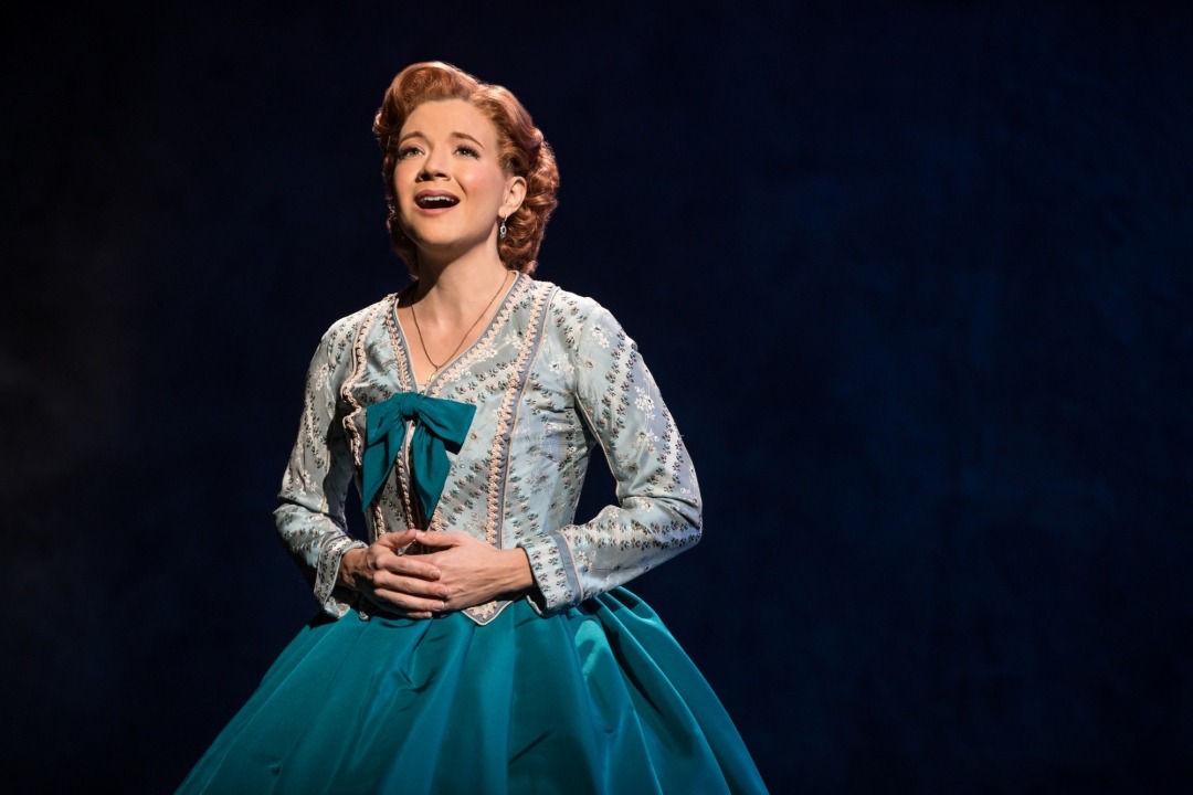 Woman in blue dress singing with a black background.