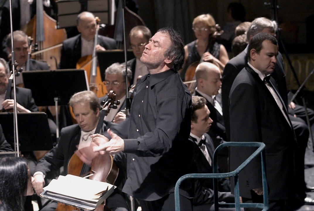 Close up of a man conducting the orchestra with strings section in the background