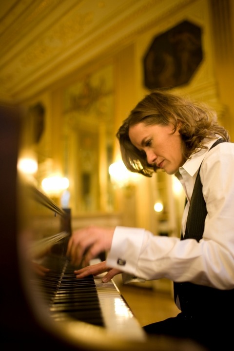 Side view of Susan Werner playing the piano with a luxurious wall behind her