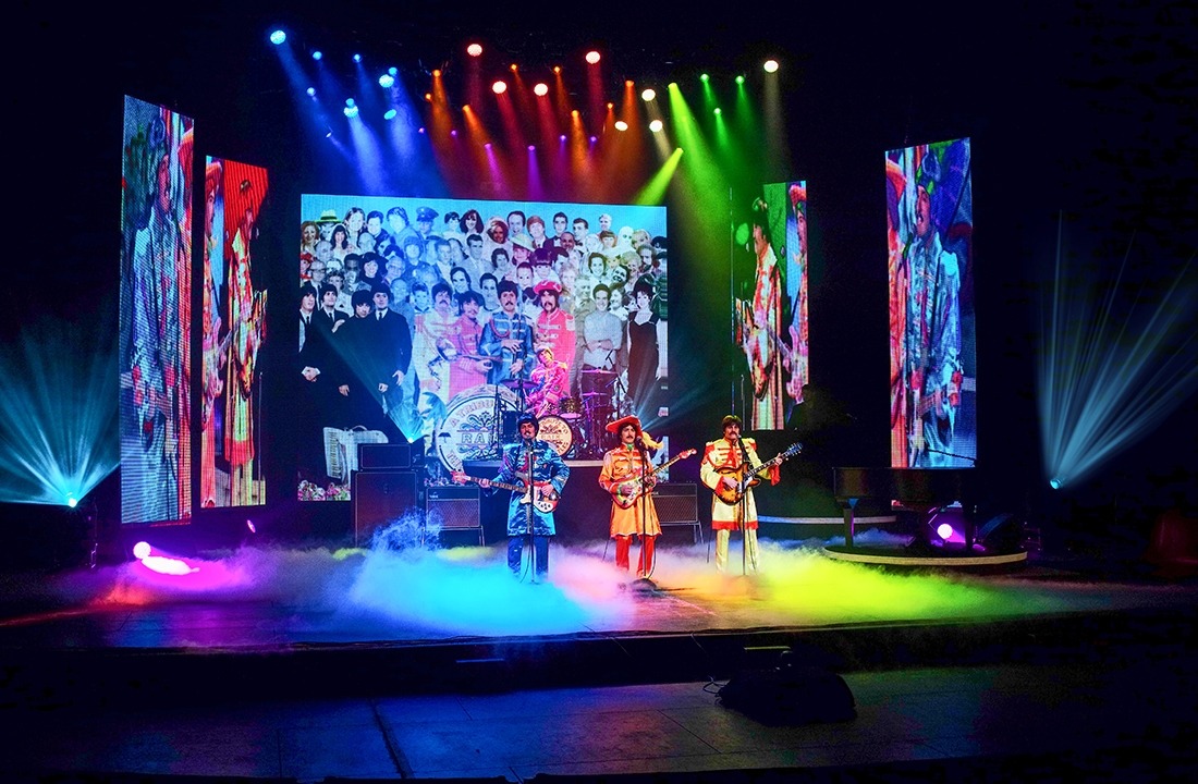 Image of the performers in RAIN on stage in colorful outfits in tribute to the Beatles of the Sgt. Pepper era.