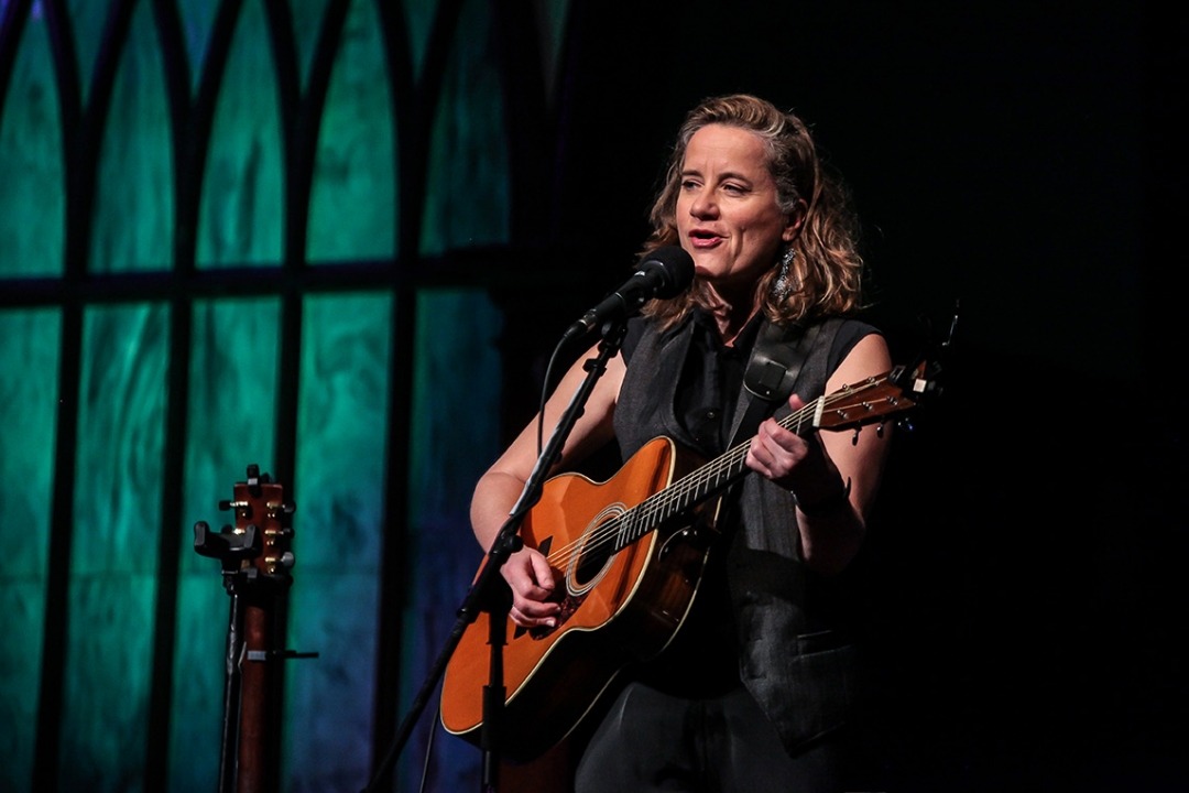 Susan Werner onstage singing into a microphone and playing her guitar