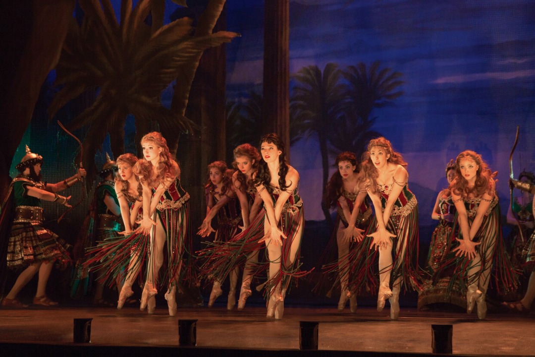 8 dancers in red and green beaded costume dancing in front of a desert background.