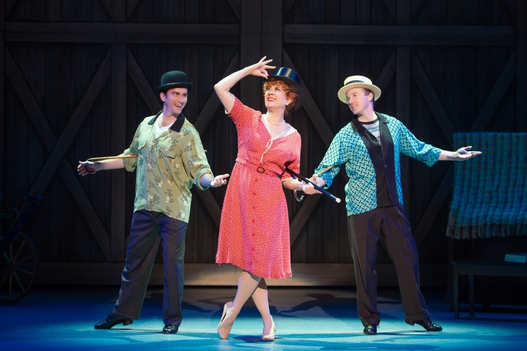 Woman in red dress with a top hat and cane posing in front of two men with hats in front of a black background