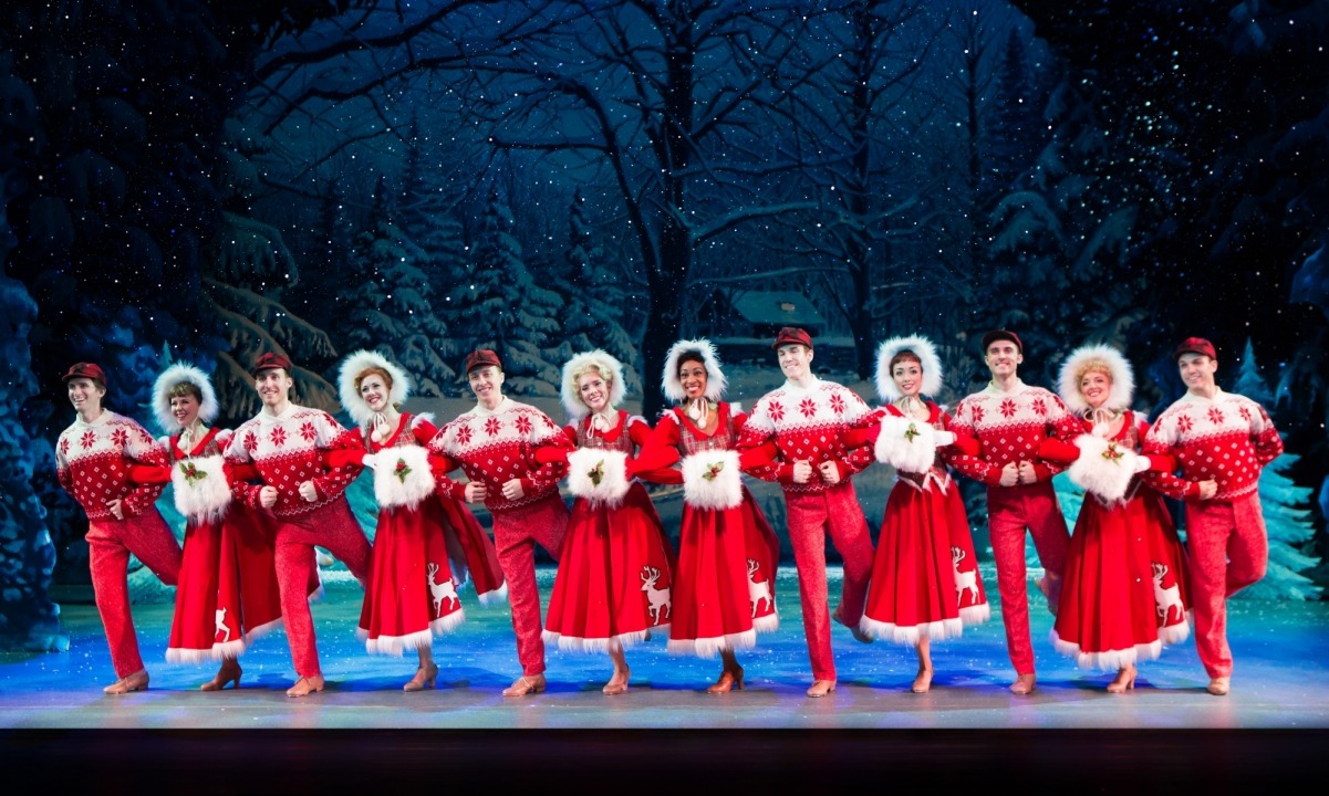 Men and women dressed in red dancing in a line in front of a snowy forest background