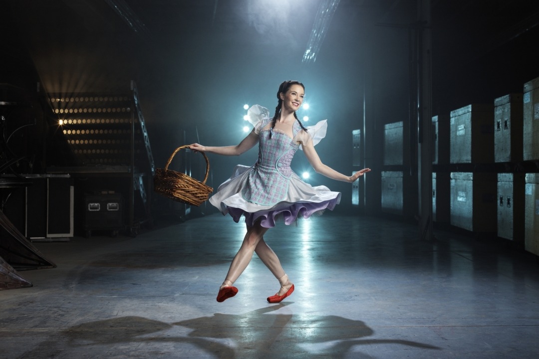 Woman in a blue dress and red shoes in a room with a blue light behind her