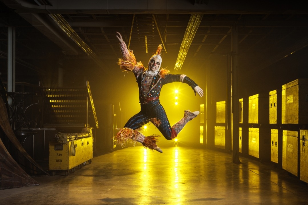 Man in a scarecrow costume jumping in a room with a yellow light in the background.