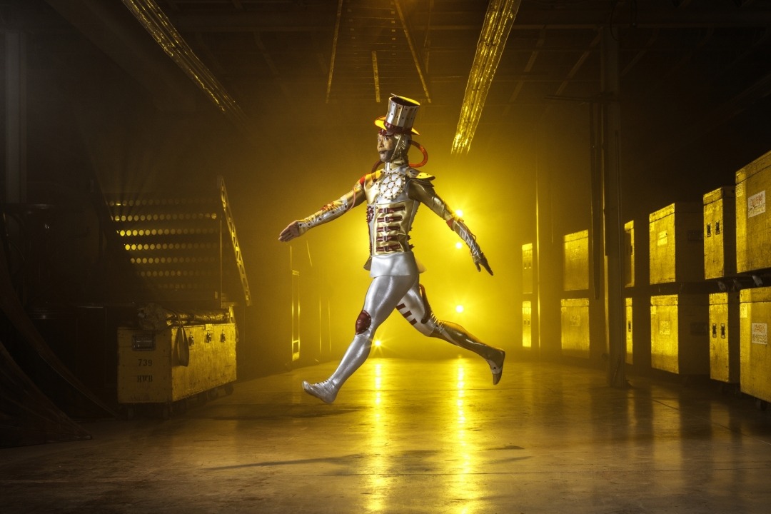 Man in a tin man costume jumping in a room with a yellow light in the background.