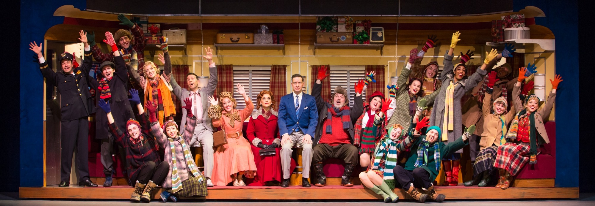 Group of people dressed in winter gear sitting together with their arms up in the air