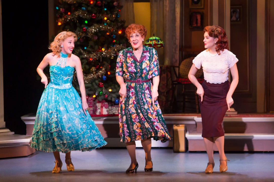 Three women dancing in a line in front of a Christmas tree