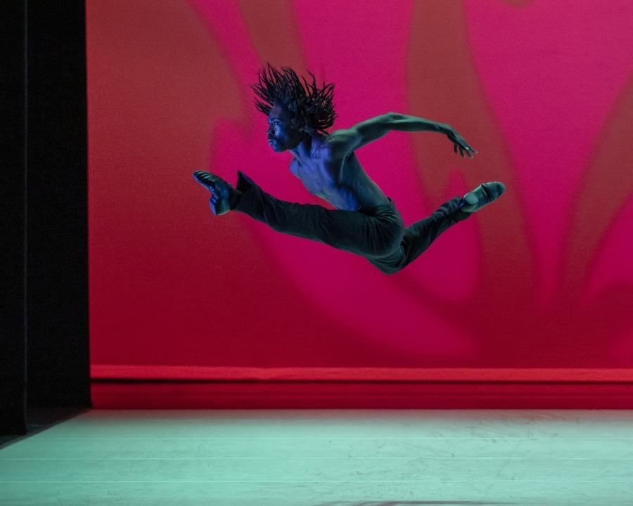 Man jumping in the air with his front leg straight and his back leg bent and his arms behind himself.