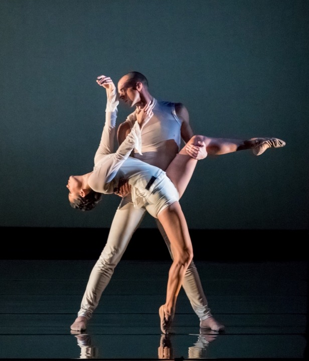 A man and woman wearing white dancing in front of a black background