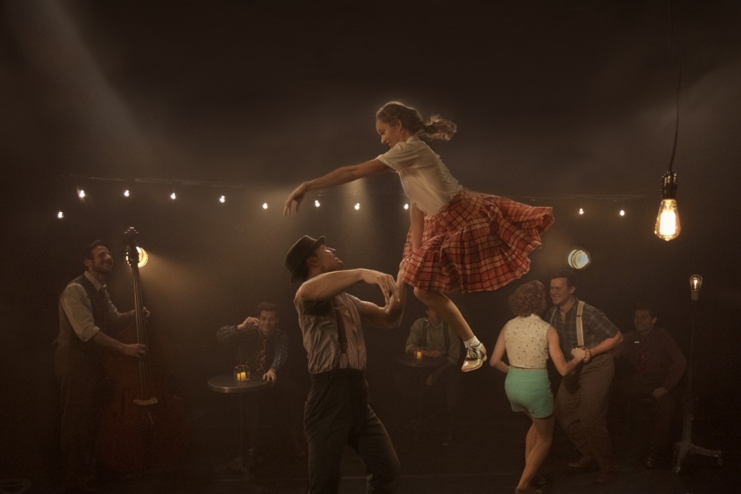 Girl in plaid skirt jumping into guys arms with people dancing in the background