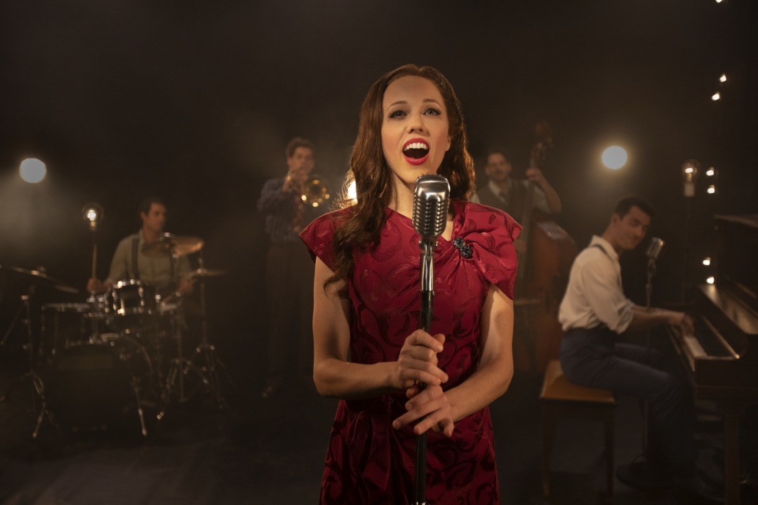 Woman in red dress singing behind a microphone in front of a band
