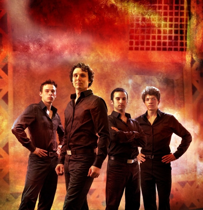 Four men in black shirts and pants standing in front of an orange background.