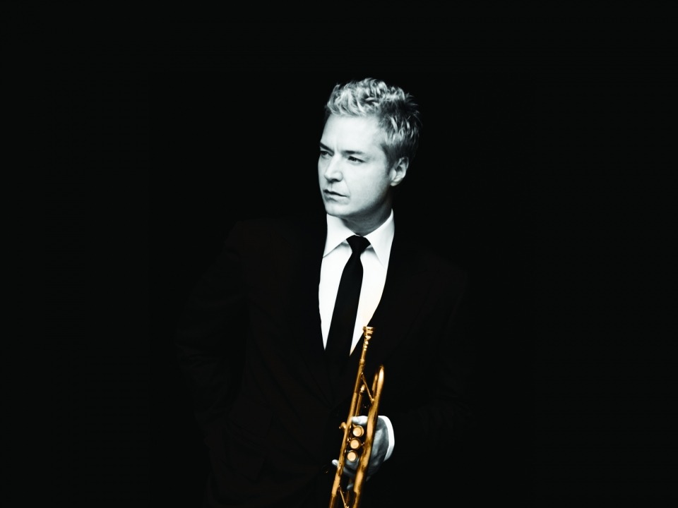Chris Botti in black and white wearing a suit and holding his trumpet that is shown in color