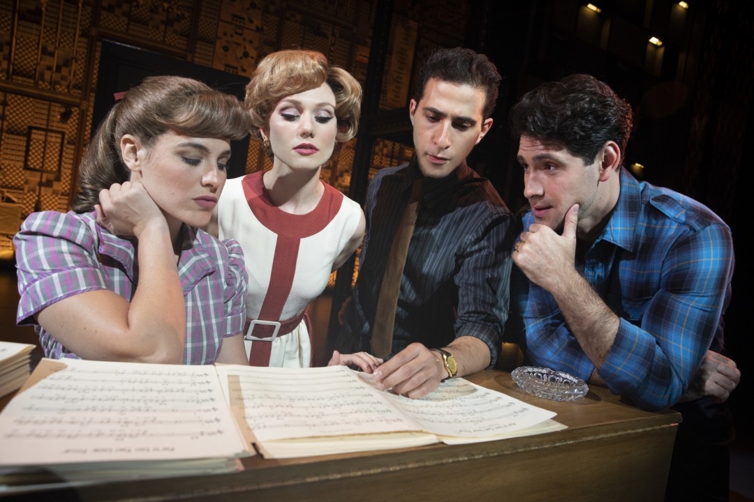 Two men and two women standing behind a piano looking at sheet music