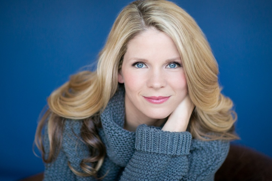 Head shot of a woman in a blue sweater in front of a blue background.