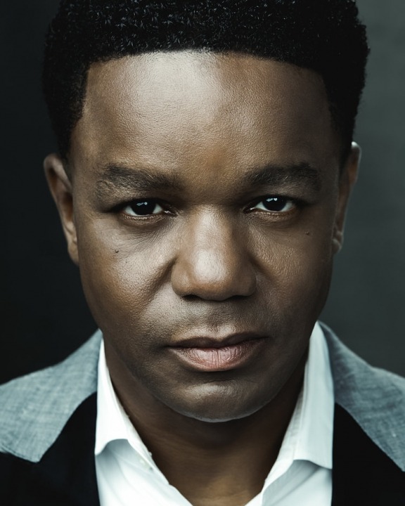 Close up shot of an African American man staring into the camera in front of a gray background.