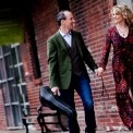 Image of the two performers from Celtic Celebration holding hands and their fiddles in cases while walking by a brick wall.