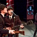 Image of the performers in RAIN on stage in black suits, white, shirts, and black ties in tribute to the early Beatles.