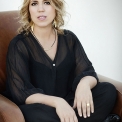 Image of Gabriela Monteri in a black shirt and pants seated on a brown chair.