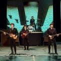 Image of the performers in RAIN on stage in black suits, white, shirts, and black ties in tribute to the early Beatles.