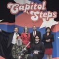 4 actors in caricature standing, 2 actors in caricature kneeling, all posing for a professional image in front of red, white, and blue background with Capitol Steps displayed overhead.