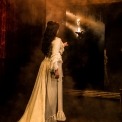 Christine in a white dress facing a mirror that shows the Phantom in black reaching out to her with fog in between them.