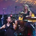 Woman playing a violin and another woman drumming behind her