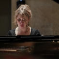 Image of Gabriela Monteri in a black shirt seated at a piano with eyes cast down toward the keys.