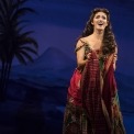 Christine in a red and green beaded dress in front of a blue-tinted desert background