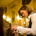 Side view of Susan Werner playing the piano with a luxurious wall behind her