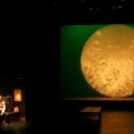 A man sitting in a room to the left of the screen. The screen projects an image of wheat