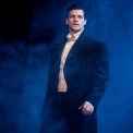 Raul in a black suit and white shirt in front of a foggy blue background.