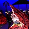 Close up of a woman in a red, traditional Mexican dress dancing with a blue background