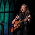 Susan Werner onstage singing into a microphone and playing her guitar