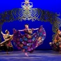 Three woman in colorful Mexican attire dance with a flora and fauna style arch in the background