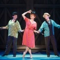 Woman in red dress with a top hat and cane posing in front of two men with hats in front of a black background