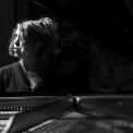 Image of Gabriela Monteri in black and white, seated at a piano glancing pensively up to her right.