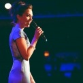 The side profile of a woman in a light blue dress singing with a dark background