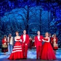 Men and women standing in couples dressed in red in front of a snowy forest background