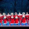 Men and women dressed in red dancing in a line in front of a snowy forest background