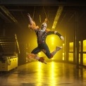 Man in a scarecrow costume jumping in a room with a yellow light in the background.