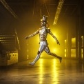 Man in a tin man costume jumping in a room with a yellow light in the background.