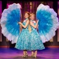 Two women in blue dresses holding big blue and white fans in front of a purple background