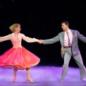 A woman in a pink dress and a man in a gray suit dancing in front of a black background