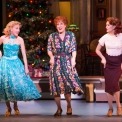 Three women dancing in a line in front of a Christmas tree