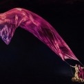 A woman in yellow and a man in red holding a string connected to a red piece of sheer fabric that's floating in front of a black background.