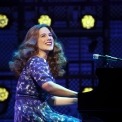 Woman in purple dress sitting at a grand piano singing in front of lights